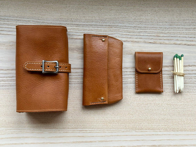 Leather goods shown from above, largest to smallest from left to right. The largest being a leather pipe case, then a leather tobacco pouch, then a small leather match case, then a bundle of hand-cut cigar or pipe matches.